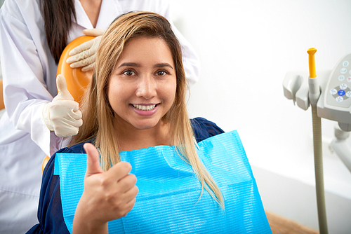 Young pretty Asian woman showing thumbs-up treating teeth
