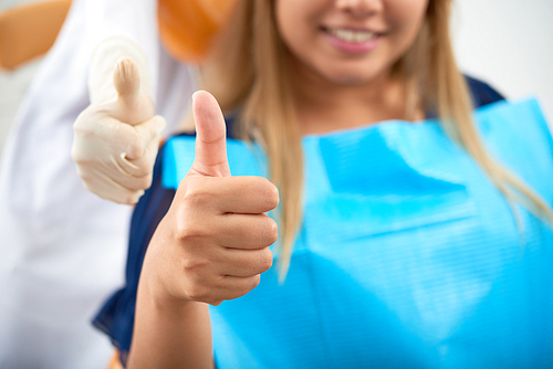 Young smiling woman and her dentist showing thumbs-up after treatment or teeth whitening