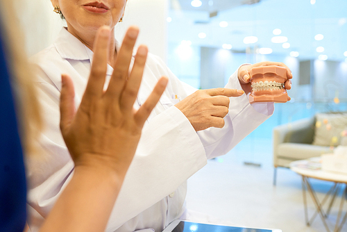 Orthodontist showing model of human jaw with braces to patient and explaining its work