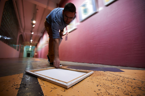 Portrait of art gallery worker picking up picture frame from floor, copy space