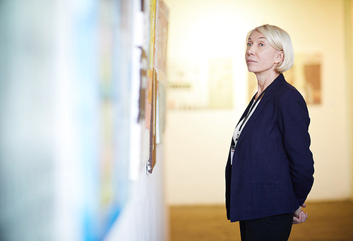 Side view portrait of pensive mature woman looking at paintings in art gallery, copy space