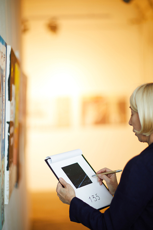 Portrait of unrecognizable woman holding clipboard taking notes on pictures in art gallery, copy space