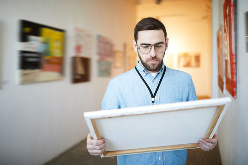 Waist up portrait of pensive bearded man holding picture in art gallery or museum, copy space