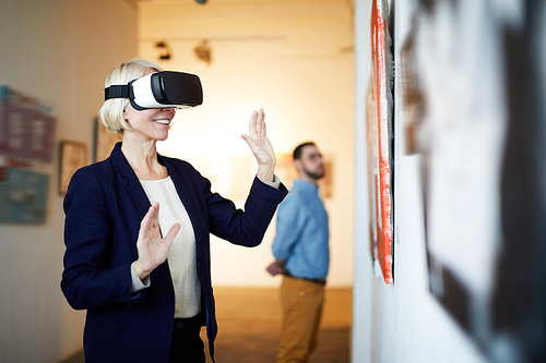 Waist up portrait of contemporary smiling woman wearing VR headset in art gallery, copy space