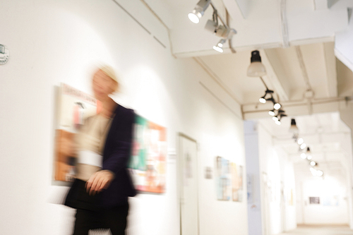 Blurred shape of unrecognizable woman walking in art gallery hall, copy space