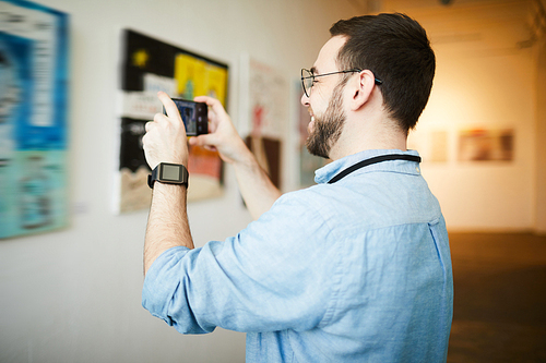 Side view  portrait of smiling  man taking smartphone photo of painting in art gallery, copy space