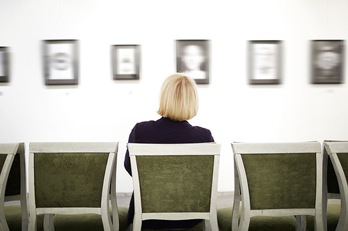 Back view portrait of elegant woman sitting on velvet chair looking at pictures in art gallery or museum, copy space