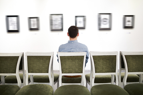 Back view portrait of unrecognizable man sitting on velvet chair looking at pictures in art gallery or museum, copy space