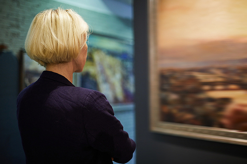 Back view portrait of unrecognizable woman looking at pictures in modern art gallery or museum, copy space