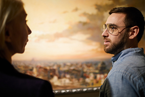 Side view portrait of two visitors discussing paintings standing in art gallery or museum, copy space