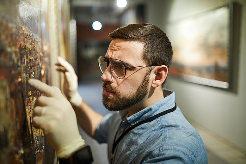 Close up  of bearded museum worker inspecting painting for restoration, copy space