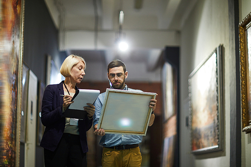 Portrait of two museum workers inspecting paintings standing in art gallery, copy space