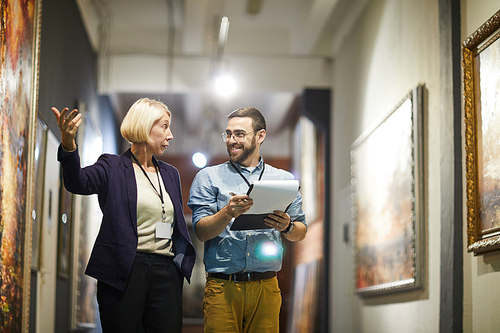 Portrait of two cheerful museum workers discussing paintings walking in art gallery, copy space