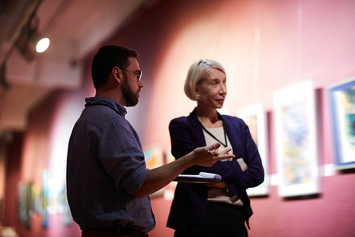 Waist up portrait of two art gallery workers inspecting paintings in museum exhibition