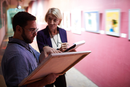 Portrait of two art gallery workers inspecting paintings in museum exhibition, copy space