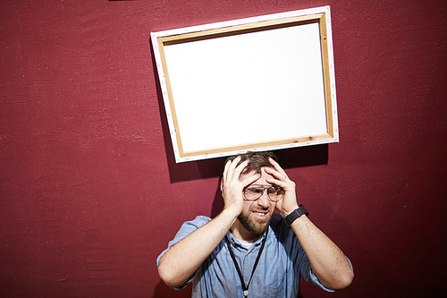 Portrait of man hit by picture frame standing against red wall shot with flash