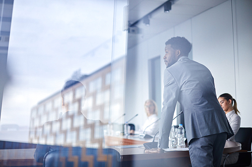 Young African-american businessman bending over table with microphone while listening to colleague during debate