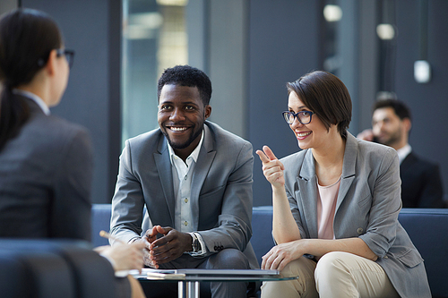 Positive confident young multi-ethnic business people sitting at table in lounge area and sharing ideas about startup project at informal meeting