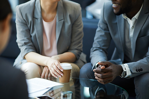 Close-up of multi-ethnic business people sitting at glassy table and discussing agreement during coffee break