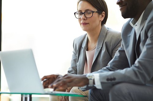 Close-up of content concentrated interracial colleagues in formal outfit sitting at coffee table and using laptop while analyzing sales statistics