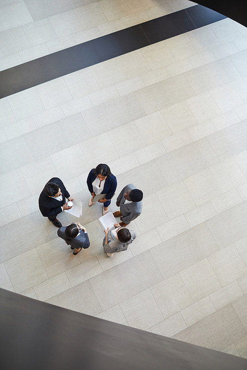 Directly above view of multi-ethnic business colleagues with papers standing in circle and brainstorming about startup project in lobby