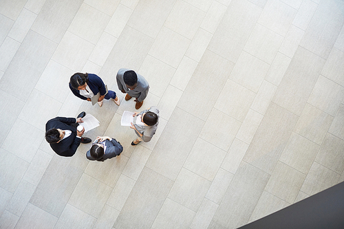 Directly above view of busy creative business colleagues in formal outfits standing in circle and discussing company issues while analyzing contracts