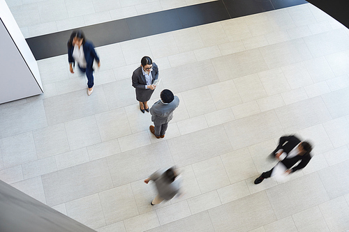 Directly above view of young multi-ethnic business partners in formal outfits standing on tile floor and chatting while meeting in corridor, blurred motion effect