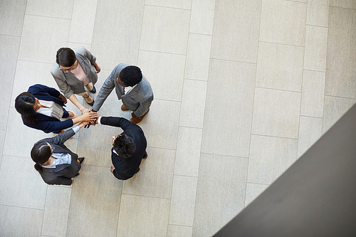 Directly above view of confident business team members in formalwear standing in circle in lobby and stacking hands together while saying motivational speech