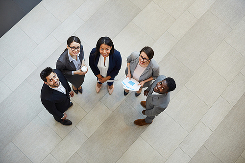 Directly above view of happy confident young multi-ethnic business professionals in formal suits standing in hall of company and smiling at camera