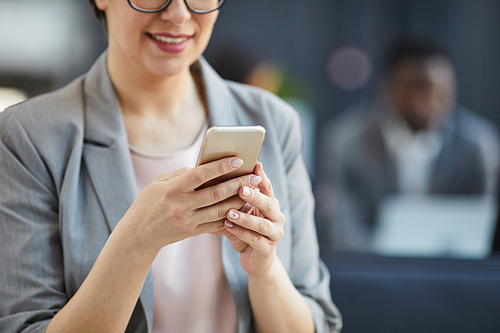 Close-up of smiling businesswoman with natural manicure using smartphone while texting message or surfing net