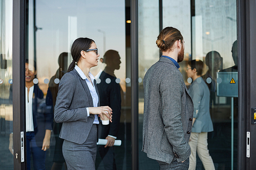 Group of modern business people in formal outfits coming in convention center through revolving door