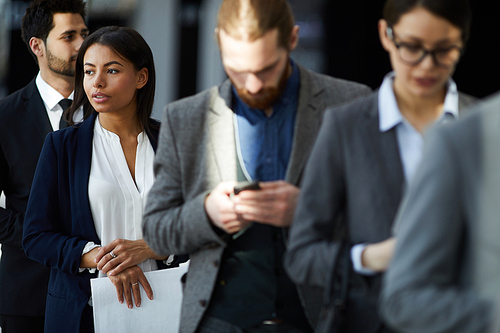 Multiethnic group of business people standing in line while applying for registration: pensive black woman looking away and holding papers