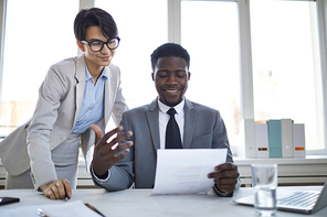 Happy director of business company in elegant suit and his secretary reading financial paper by workplace