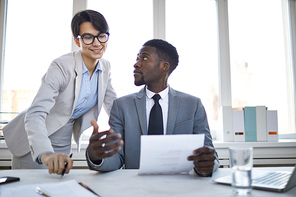 Confident businessman in suit showing contract to colleague and explaining its main points at meeting