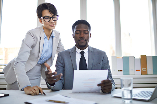 Young confident boss in elegant suit looking though text of contract typed by his secretary while sitting in office