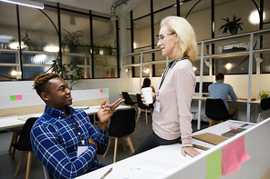 Content multi-ethnic business colleagues discussing ideas for new project: mature lady drinking coffee and listening to ambitious black manager