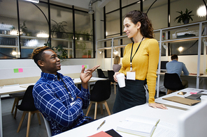 Positive young multi-ethnic colleagues with badges exchanging ideas while chatting during break in modern office