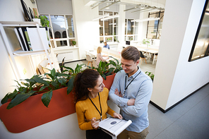 Content confident attractive young lady with clipboard presenting statistical chart to colleague while they standing in corridor of modern coworking space