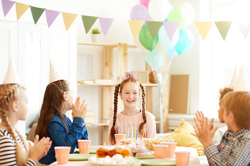 Group of children celebrating birthday at party table with happy red haired girl in center, copy space
