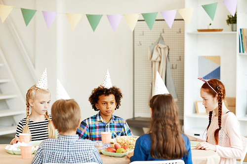 Multi ethnic group of children celebrating birthday sitting at table in cafe, focus on African-American boy, copy space