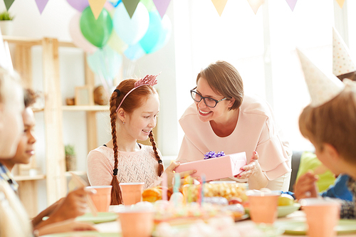 Portrait of smiling mother giving Birthday present to daughter during party, copy space