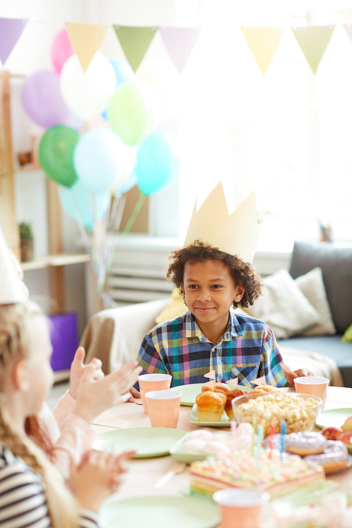 Portrait of smiling African-American boy wearing crown sitting at table while celebrating Birthday with friends