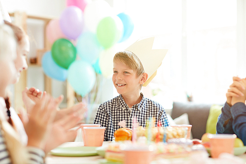 Portrait of smiling boy wearing crown sitting at table while celebrating Birthday with friends, copy space