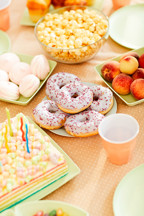 High angle closeup of Birthday party table with delicious sweet food for kids, focus on plate of glazed donuts, copy space