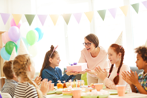 Portrait of excited little girl  receiving gifts during Birthday party with friends, copy space