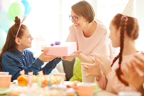 Portrait of happy girl  receiving gift from mom during Birthday party with friends, copy space