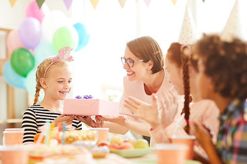 Portrait of cute little  girl  receiving gift from mom during Birthday party with friends, copy space