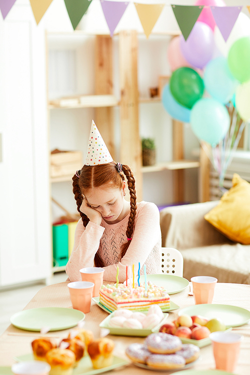 Portrait of red haired teenage girl sitting alone at party table in decorated room, copy space