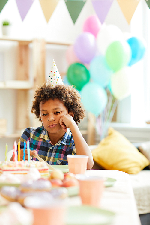 Portrait of sad African-American boy sitting at table alone during Birthday party, copy space