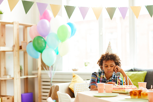 Portrait of sad African-American boy sitting alone at Birthday party in decorated room, copy space